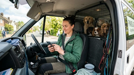 Dog walker checking their schedule on their phone in their van